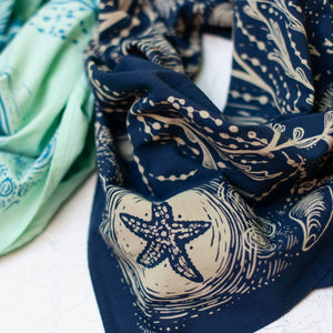 Two bandanas, one green and one blue with starfish pattern, on a white surface.