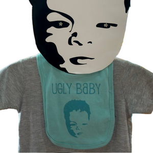 A cardboard head of the Ugly Baby logo is on a mannequin wearing a teal bib that has the Ugly Baby logo on it.