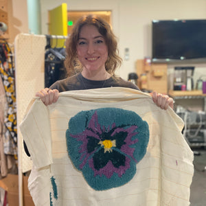 Person holding a tufted art piece with a floral design in a store setting.