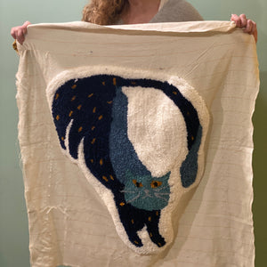 Woman holding a large white fabric with a black cat design tufted on it.