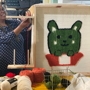 Person working on a rug with a green bear design in a workshop setting.