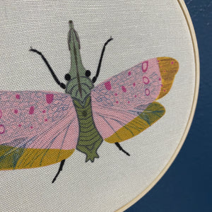 Embroidery hoop with a colorful moth design on fabric.