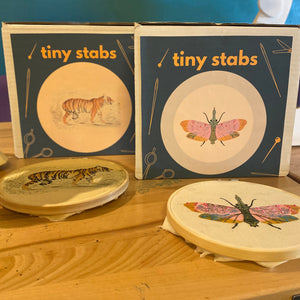 Two embroidery kits titled 'tiny stabs' with illustrations of a tiger and a moth, accompanied by completed, embroidered samples of the designs.