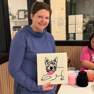 Person holding a punch needle portrait of a dog in a casual setting.
