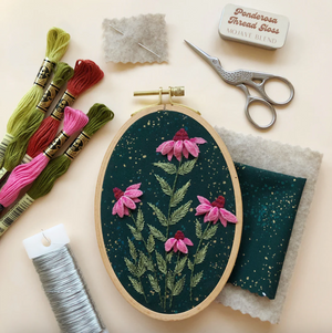 Embroidery hoop with floral design, threads, scissors, and thread gloss on a beige background.