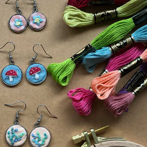 Embroidered earrings with colorful thread spools on a brown surface.