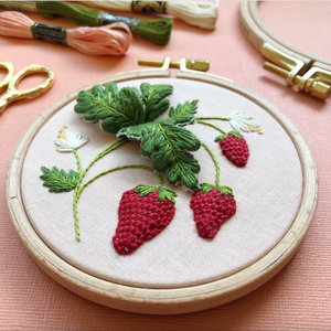 Embroidery hoop with embroidered strawberries and leaves on a pink background