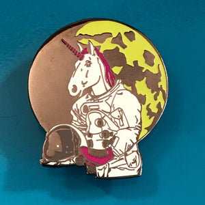An enamel pin of an astronaut unicorn wearing roller skated with a moon in the background.