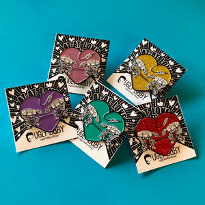 Five heart shaped enamel pins called Love AT-AT First Sight with gold, pink, red, aqua and purple backgrounds. Shown on a backing cards with hearts.