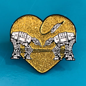 Heart shaped enamel pin called Love AT-AT First Sight with a gold glitter background.