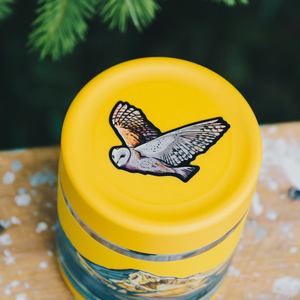 Yellow lid with the bonus owl design on a glass jar against a natural background.