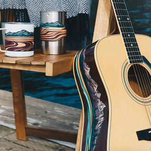 Acoustic guitar leaning against a wooden table. An Olympic National Park sticker has been applied to the side.