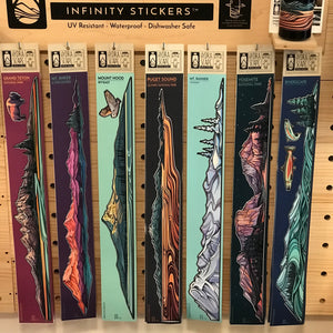Six packaged mountain and canyon landscape stickers displayed on a pegboard under a sign reading 'Infinity Stickers.' The stickers feature illustrated vertical rock formations in different colors, including teal, pink, orange, gray, and blue, with small fish illustrations on two of the packages.