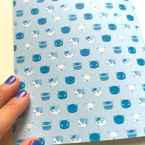 Sheet of paper with blue and white cat pattern held by a hand.
