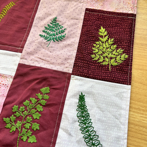 Patchwork fabric with embroidered green leaves on a wooden surface.