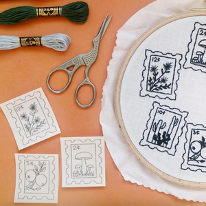 Embroidery hoop with floral designs, scissors, and thread on a peach-colored surface.