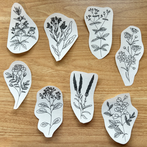 Set of white cut-out shapes with black natural dye plant patterns on a wooden surface.