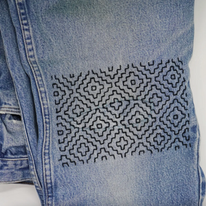 Close-up of blue denim fabric with geometric black embroidery on a white background