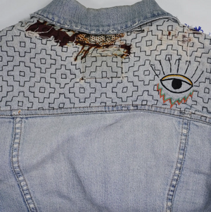 Denim jacket with visible mending designs on a white background.
