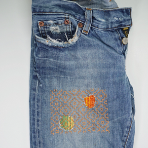 Blue jeans with embroidered designs on a white background.