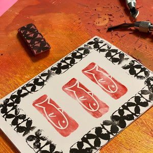 Handmade stamp with red fish design on a wooden surface.