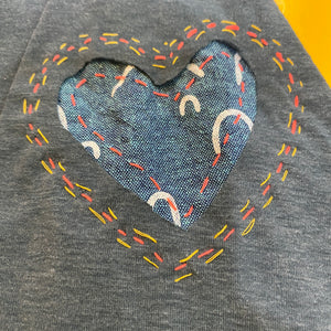 Heart-shaped reverse applique on a gray fabric background with colorful stitching.