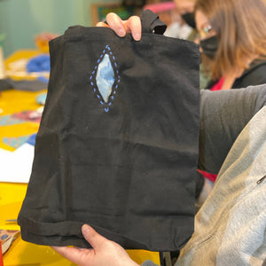 Person holding a black garment with a decorative reverse applique element in an indoor setting.