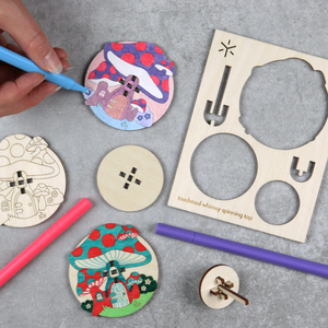 Wooden spinning tops with toadstools are being colored in with markers.
