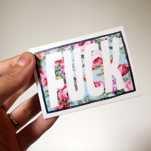 Card with floral design and the word 'FUCK' held by a hand.