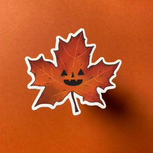 Maple leaf with a jack-o'-lantern face on an orange background.