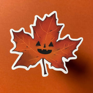 Maple leaf with a jack-o'-lantern face on an orange background.