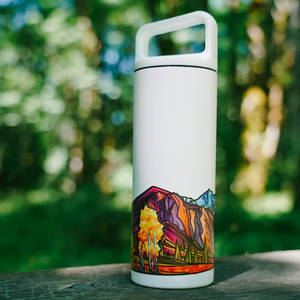White water bottle with colorful mountain design on a wooden surface with a blurred green background.