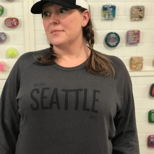 A person wearing a baseball cap and a gray sweatshirt that says "This says Seattle on it"