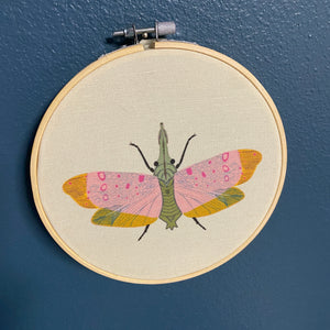 Embroidery hoop with a colorful moth design on a blue wall.
