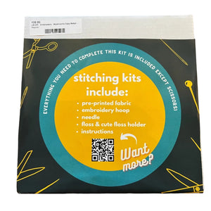 A square product box for an embroidery kit. The box has a dark forest freen background with a large yellow circular label and teal accents, plus small yellow line drawings of scissors and sewing tools.