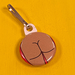 Small round zipper pull with a square butt on a yellow surface.