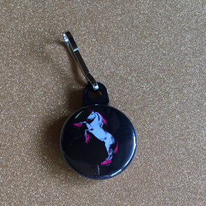 A zipper pull with a roller skating unicorn on a black background.