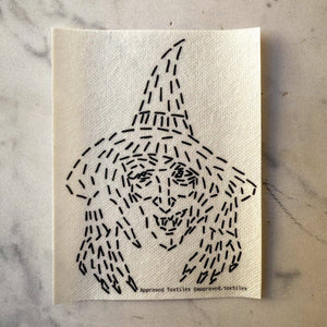 Visible mending pattern sticker featuring a witch wearing a pointy hat with her hands reaching toward the viewer