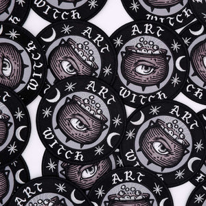 A grouping of circular patches that feature stars, crescent moons, a cauldron with an eye on it in the center, and text that says "Art Witch"