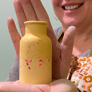 Person holding a yellow bottle with terrazzo design, wearing a floral apron.