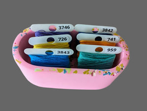 Pink container with colorful embroidery floss and labels on a light pink background.