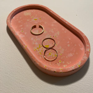 Pink speckled terrazzo jewelry dish with gold rings on a light background.