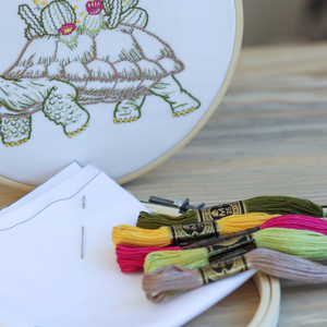 Embroidery hoop with a turtle design and colorful embroidery threads on a wooden surface.