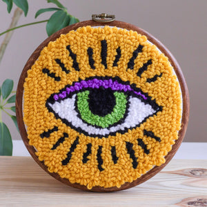 Embroidery hoop with a colorful eye punch needle design on a wooden surface.