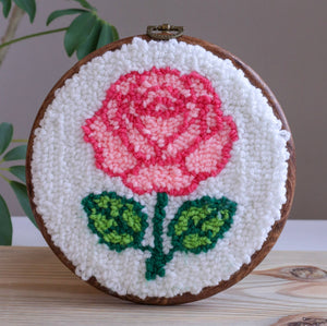 Embroidery hoop with a pink rose design on a white background