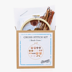 Cross stitch kit packaging with contents displayed, including an embroidery hoop, threads, a pattern, and cloth.