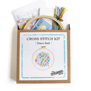 A kraft brown box that the disco ball cross stitch kit comes in. The supplies that are included in the kit are coming out the top.
