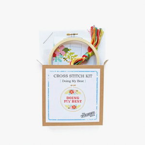 Cross stitch kit with hoop and thread on a white background. It says "Doing my best" and the supplies included in the kit are coming out of the top of the box.