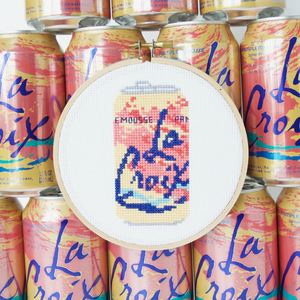 Cross-stitched design of a La Croix can surrounded by actual La Croix cans.