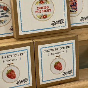 Cross stitch kits with stitched designs on cardboard boxes.